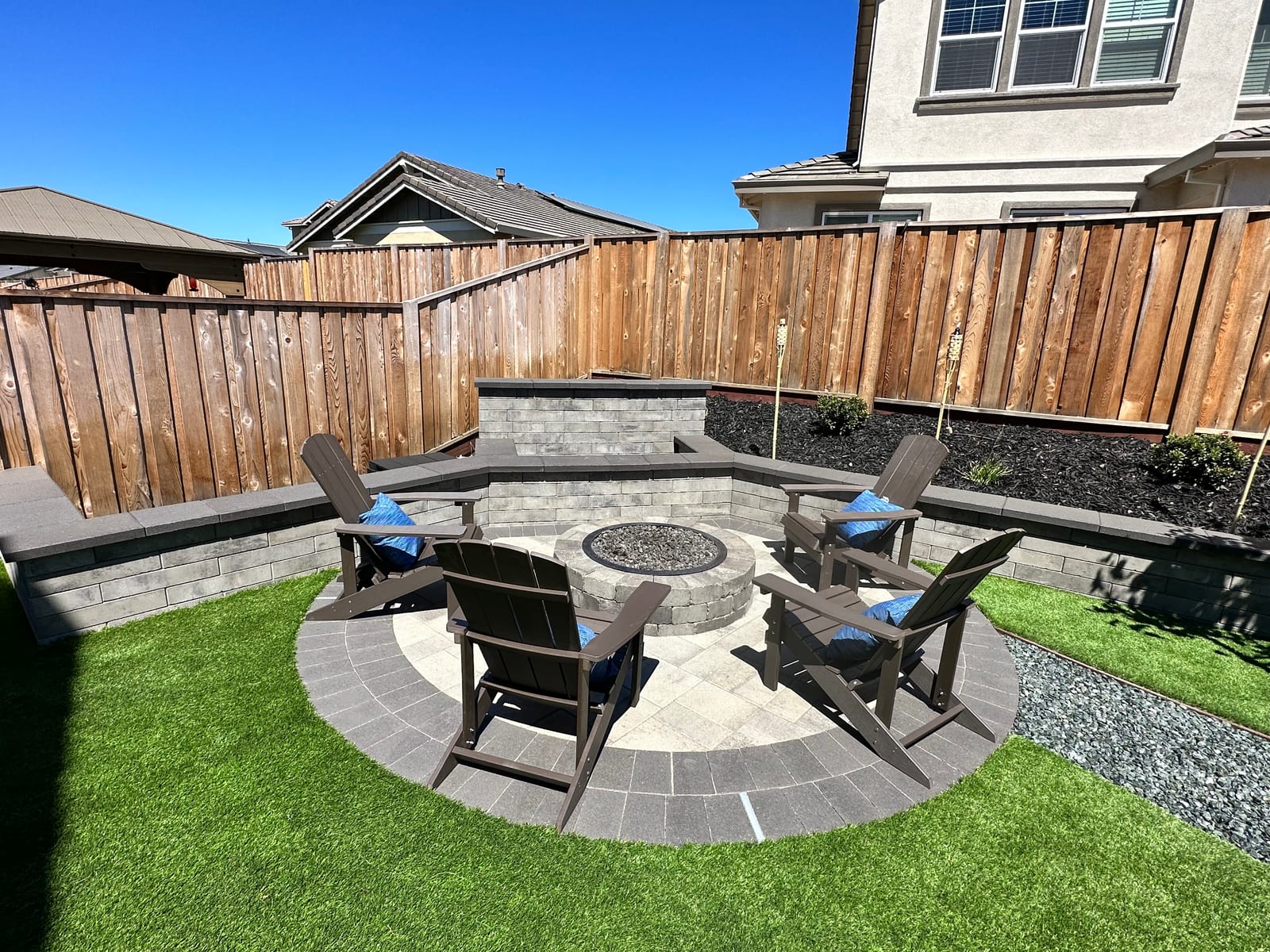 Circular paver patio with a built-in fire pit and a curved block seat wall installed by Royal Outdoor Solutions