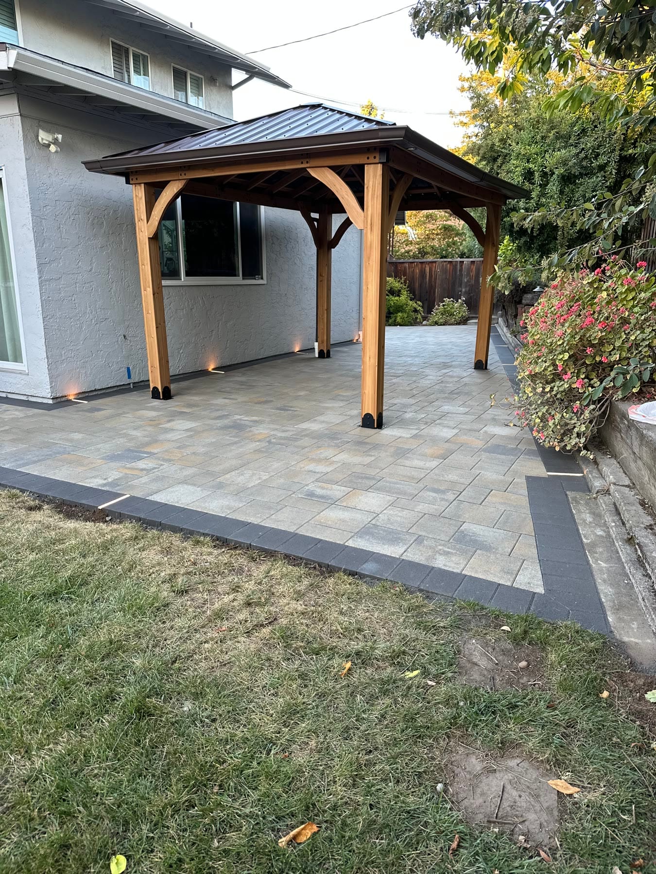 Paver patio with a dark soldier-course border and a wood pavilion installed by Royal Outdoor Solutions in Sunnyvale, CA